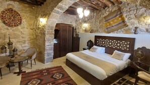 A traditional room with stone walls, a bed with a patterned headboard, a small table with chairs, and decorative lanterns. - Hayat Zaman Hotel & Resort (At-Taybeh)