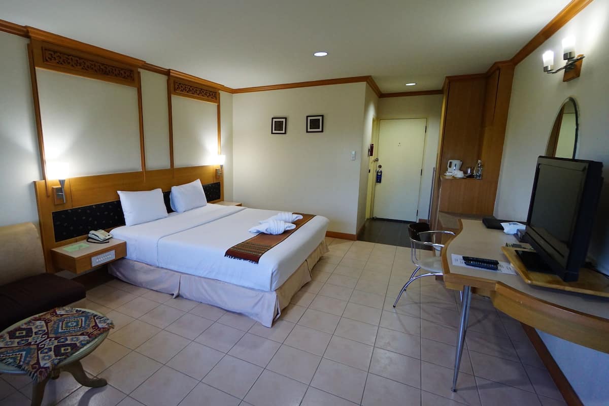 A hotel room with a bed, bedside table, chair, desk, television, and a small table with a patterned tablecloth.