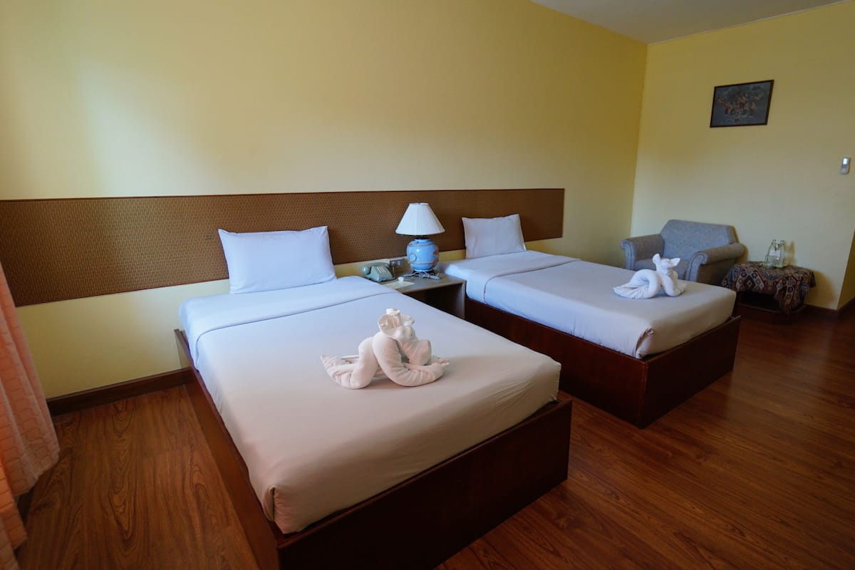 A hotel room with two beds, a nightstand with a lamp, a chair, and a small table with a vase.