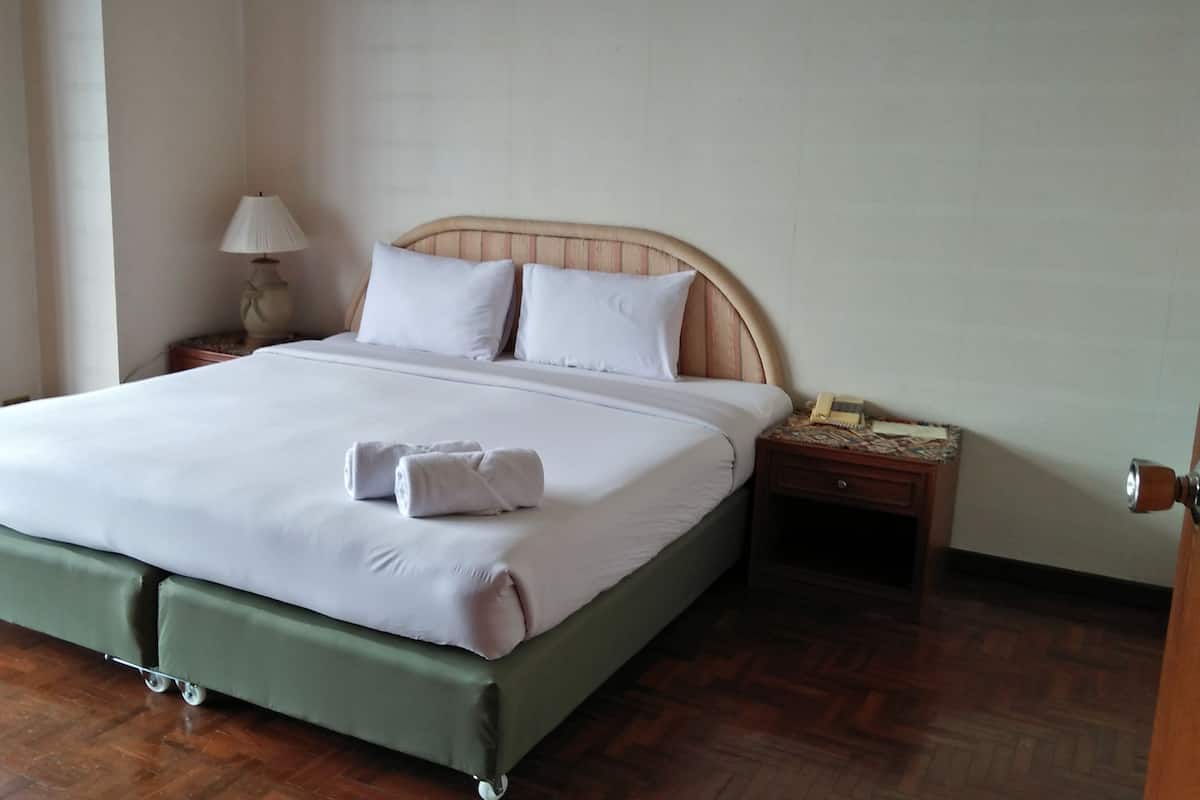 A neatly made bed with a wooden headboard, a bedside table with a lamp, and a green upholstered footboard.
