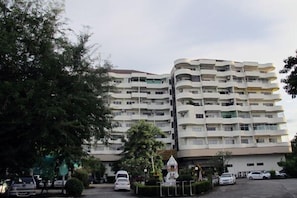 A multi-story residential building with balconies, surrounded by trees and parked cars.