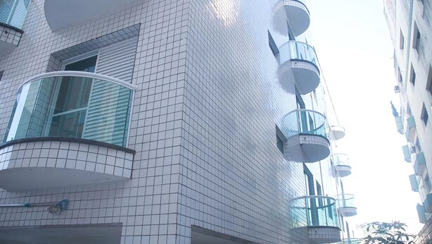 En moderne bygning med en facade af fliser, altaner med glasgelændere og en klar himmel.