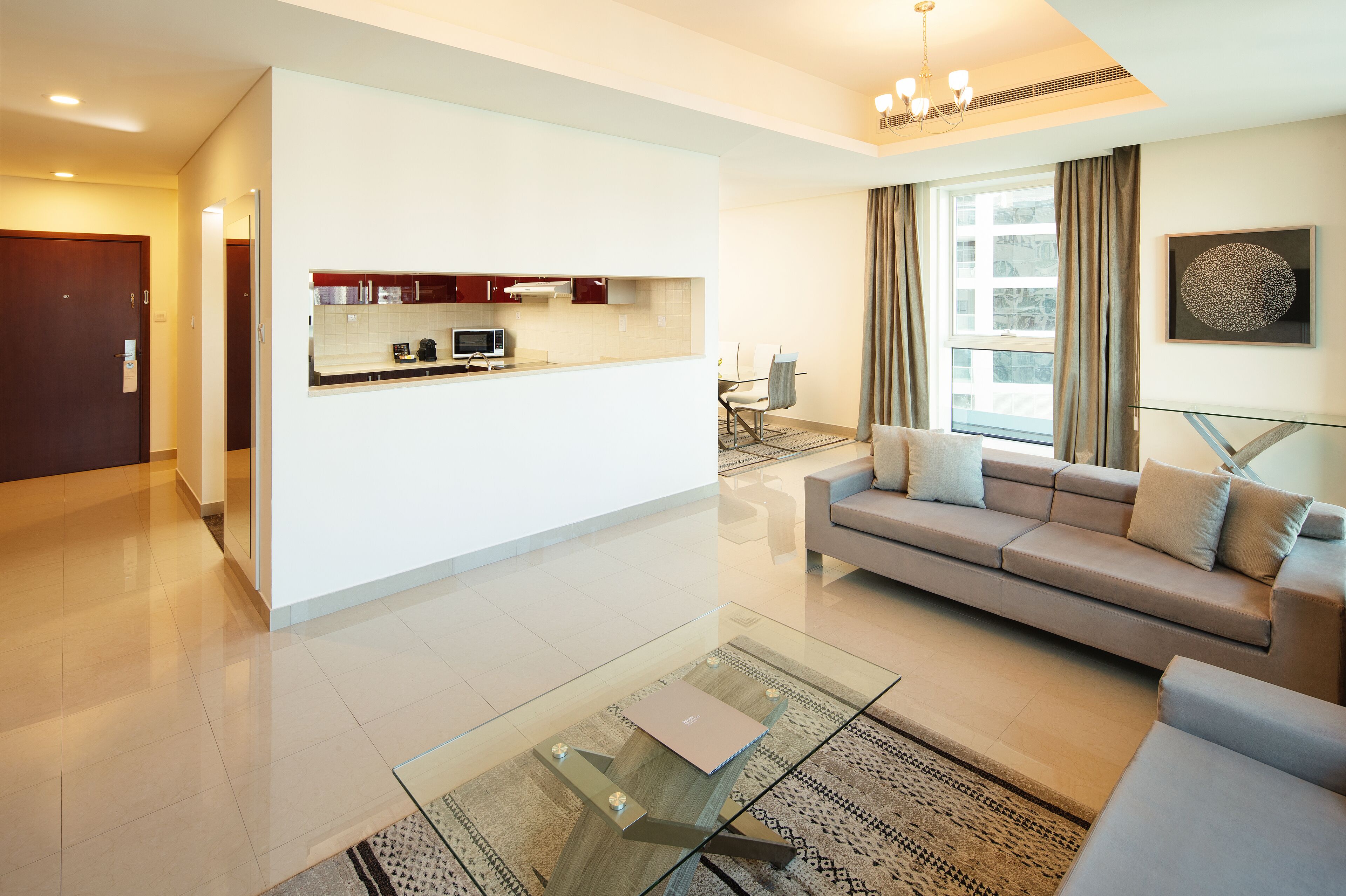 A modern living room with a sofa, a glass coffee table, and a kitchen area with cabinets and a dining table.