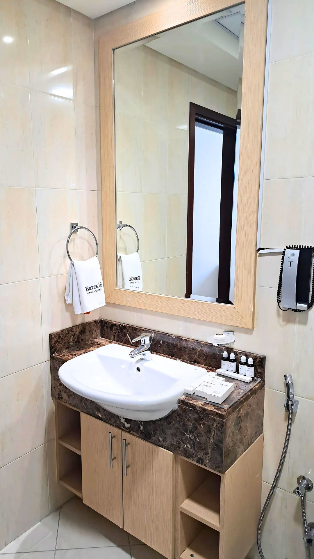 A bathroom with a white sink, marble countertop, wooden cabinets, a large mirror, and a towel rack with a white towel.