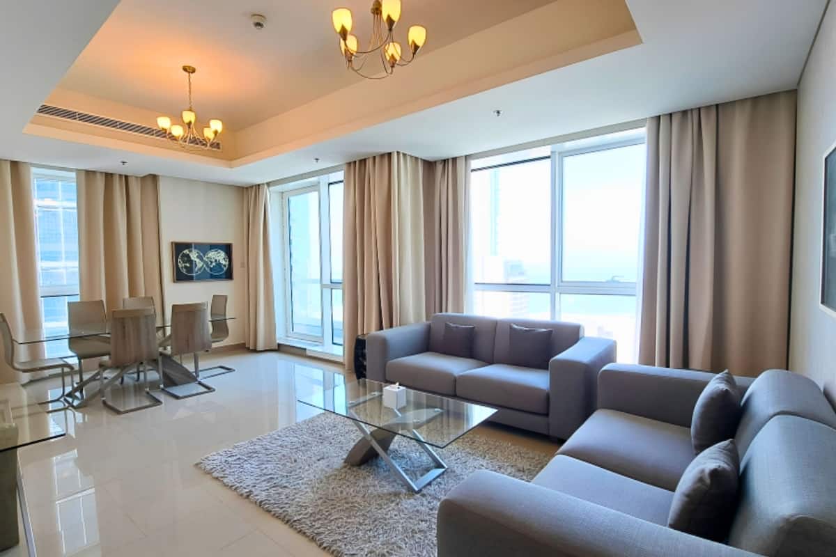 A modern living room with a glass coffee table, a grey sofa, and a dining area with chairs and a table.