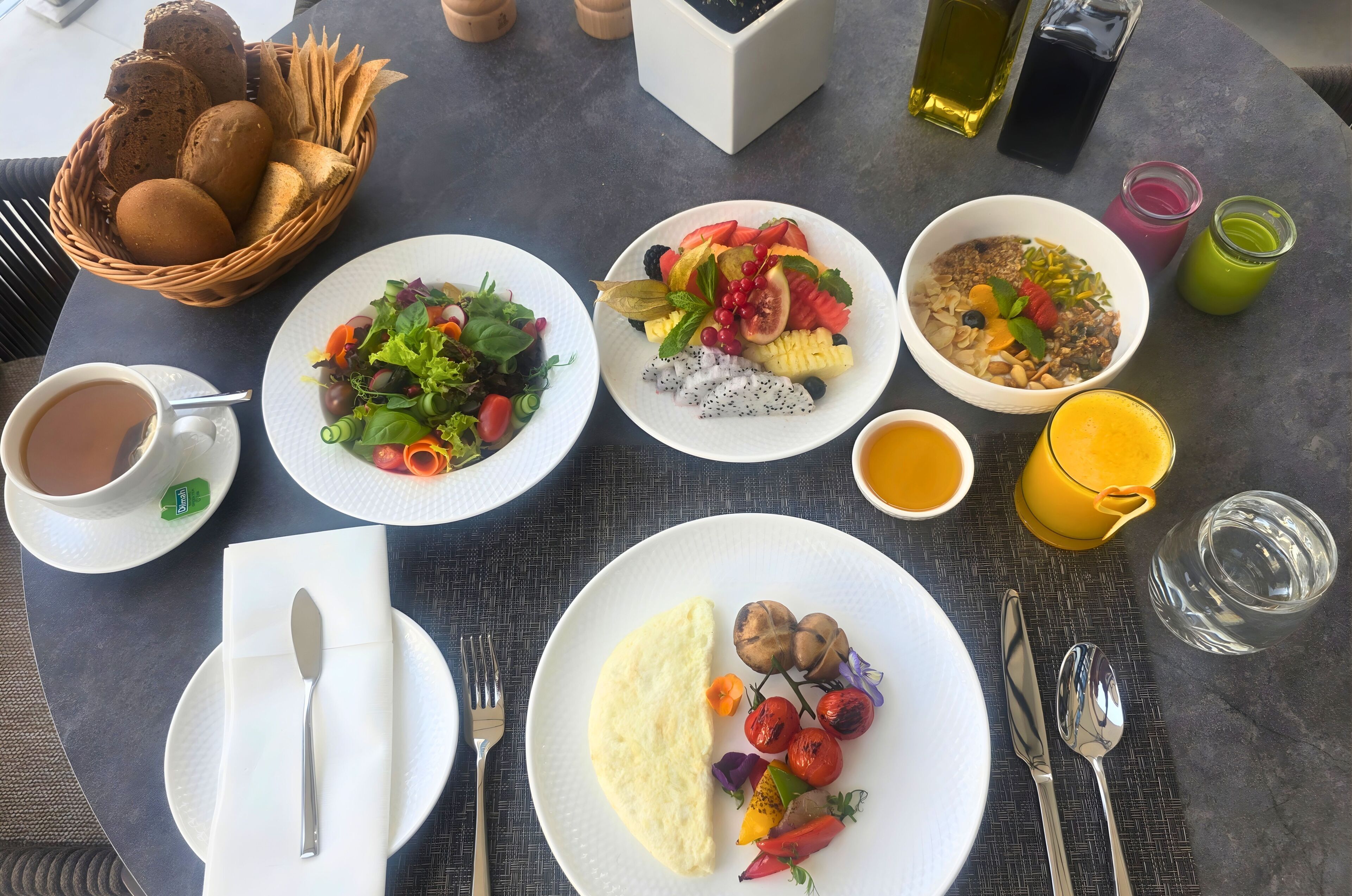 Une table dressée avec des aliments pour le petit-déjeuner, notamment du pain, de la salade, des fruits et des boissons.