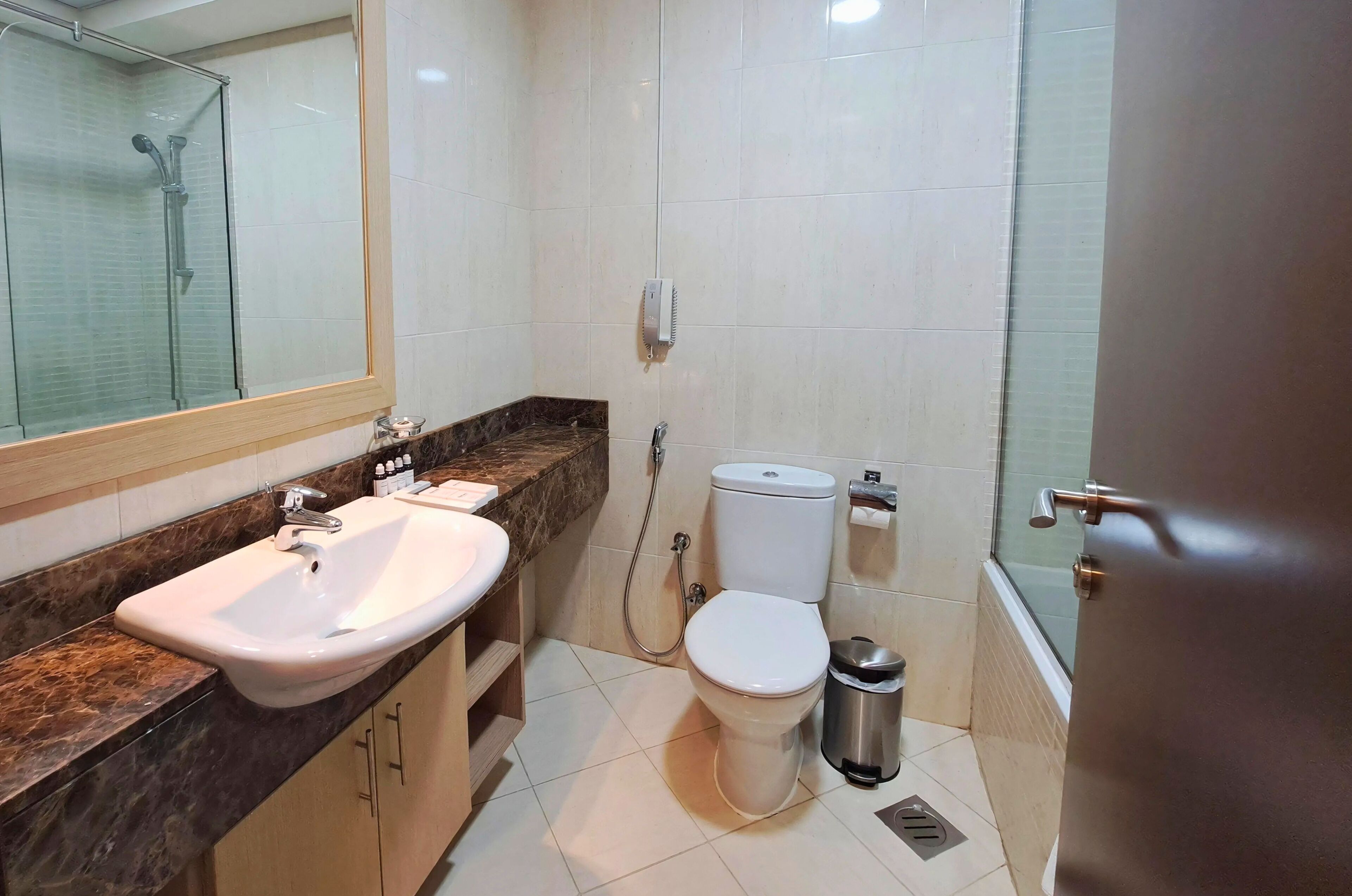 A bathroom with a sink, toilet, shower, and a trash bin.