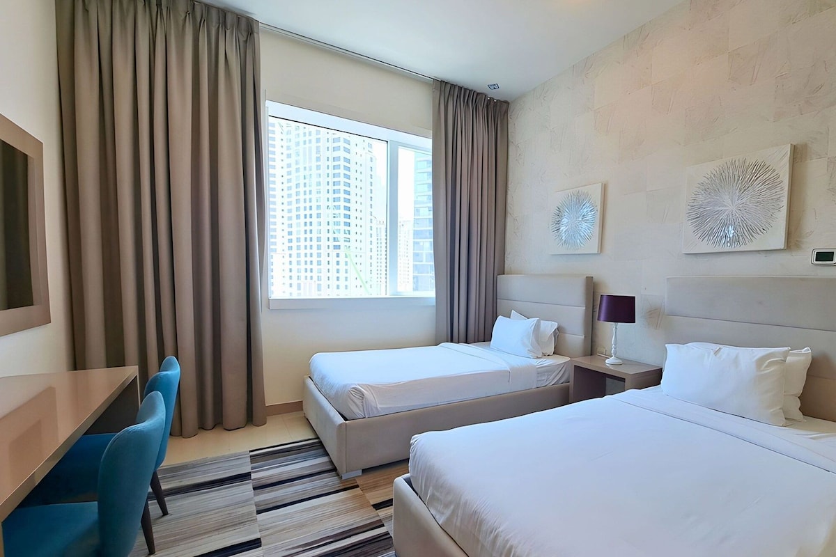 A hotel room with two beds, a desk, and a chair.