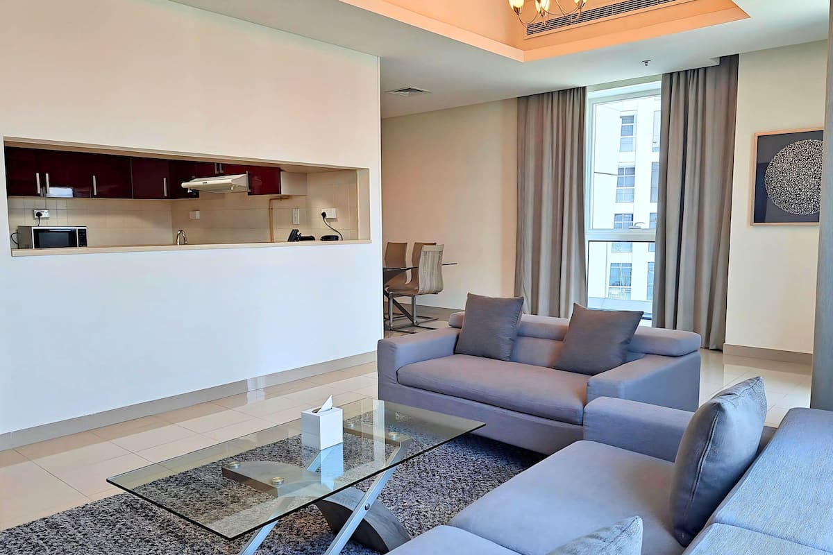 A modern living room with a sofa, a glass coffee table, and a kitchen area with cabinets and a microwave.