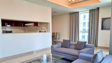 Una sala de estar moderna con un sofá, una mesa de centro de vidrio y una zona de cocina con armarios y un microondas.