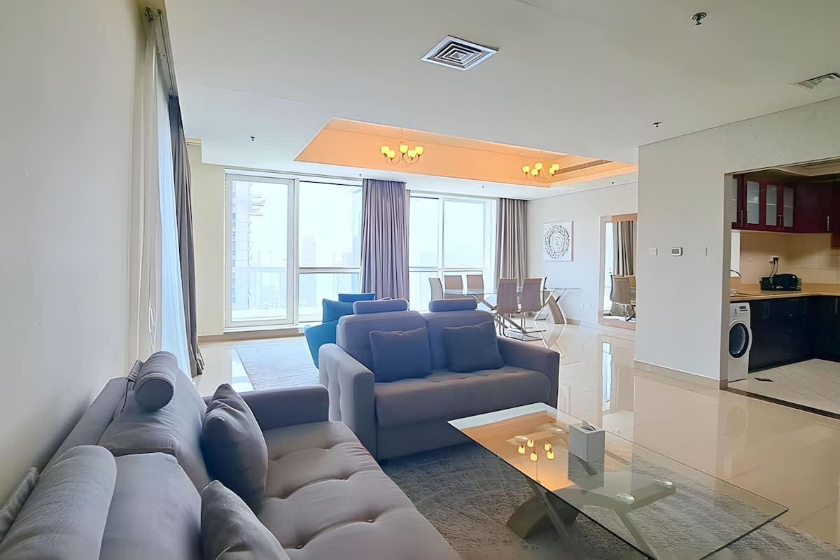 A modern living room with a grey sofa, a glass coffee table, and a dining area with a table and chairs.