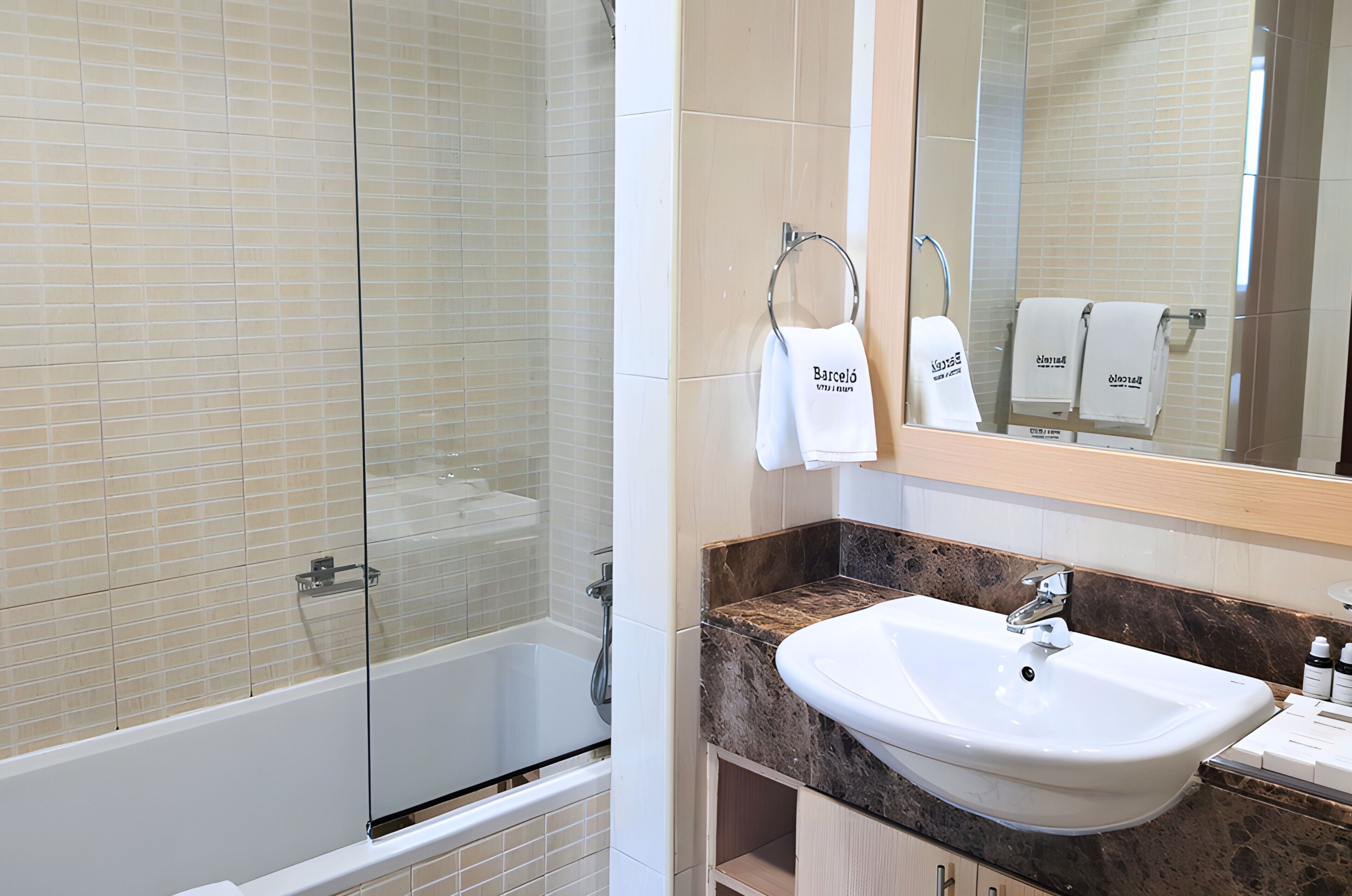 Une salle de bain avec une douche à parois de verre, un lavabo blanc et un miroir sur lequel sont accrochées deux serviettes.