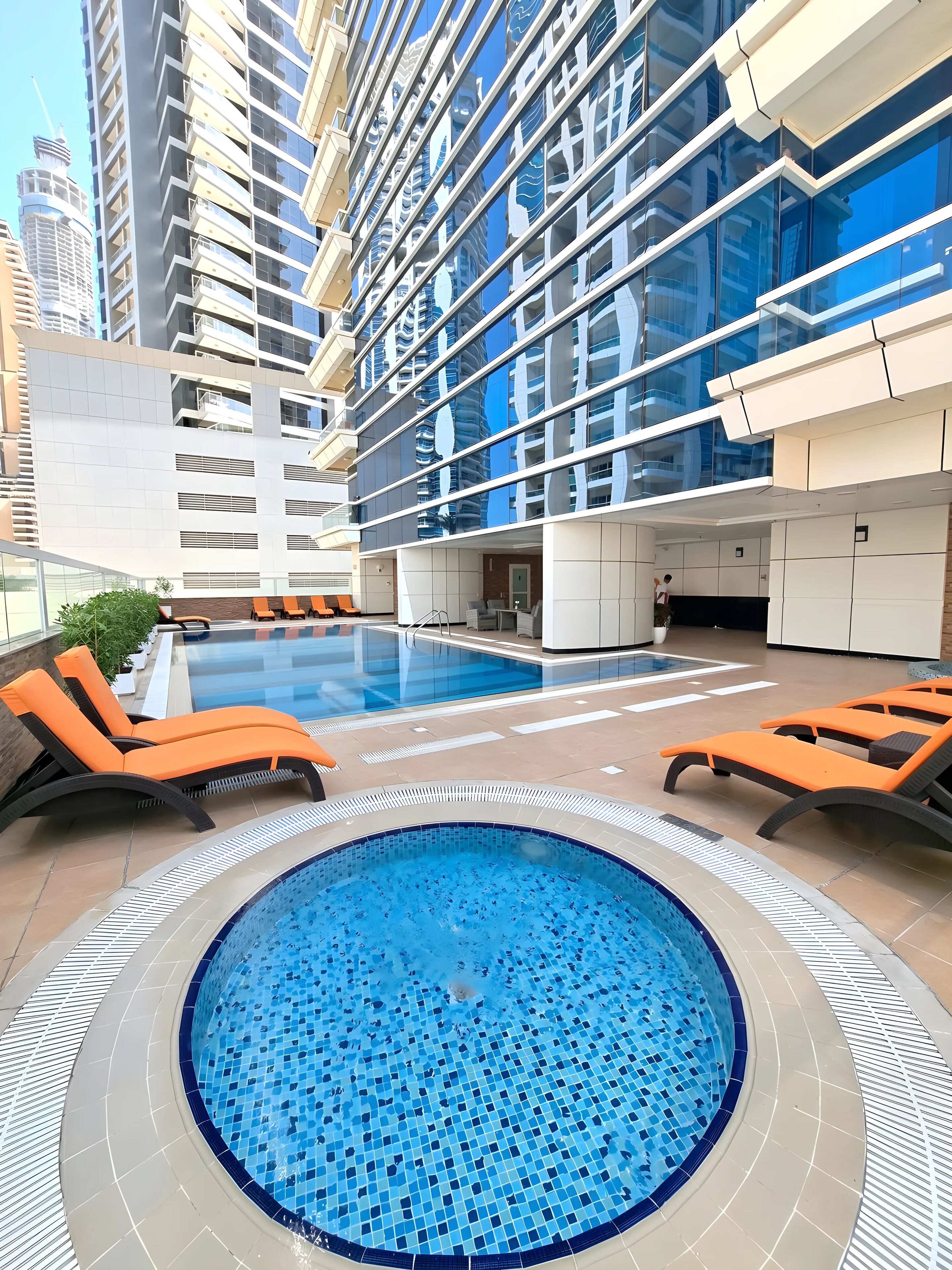 Area piscina sul tetto con poltrone relax, vasca idromassaggio e vista su moderni grattacieli.