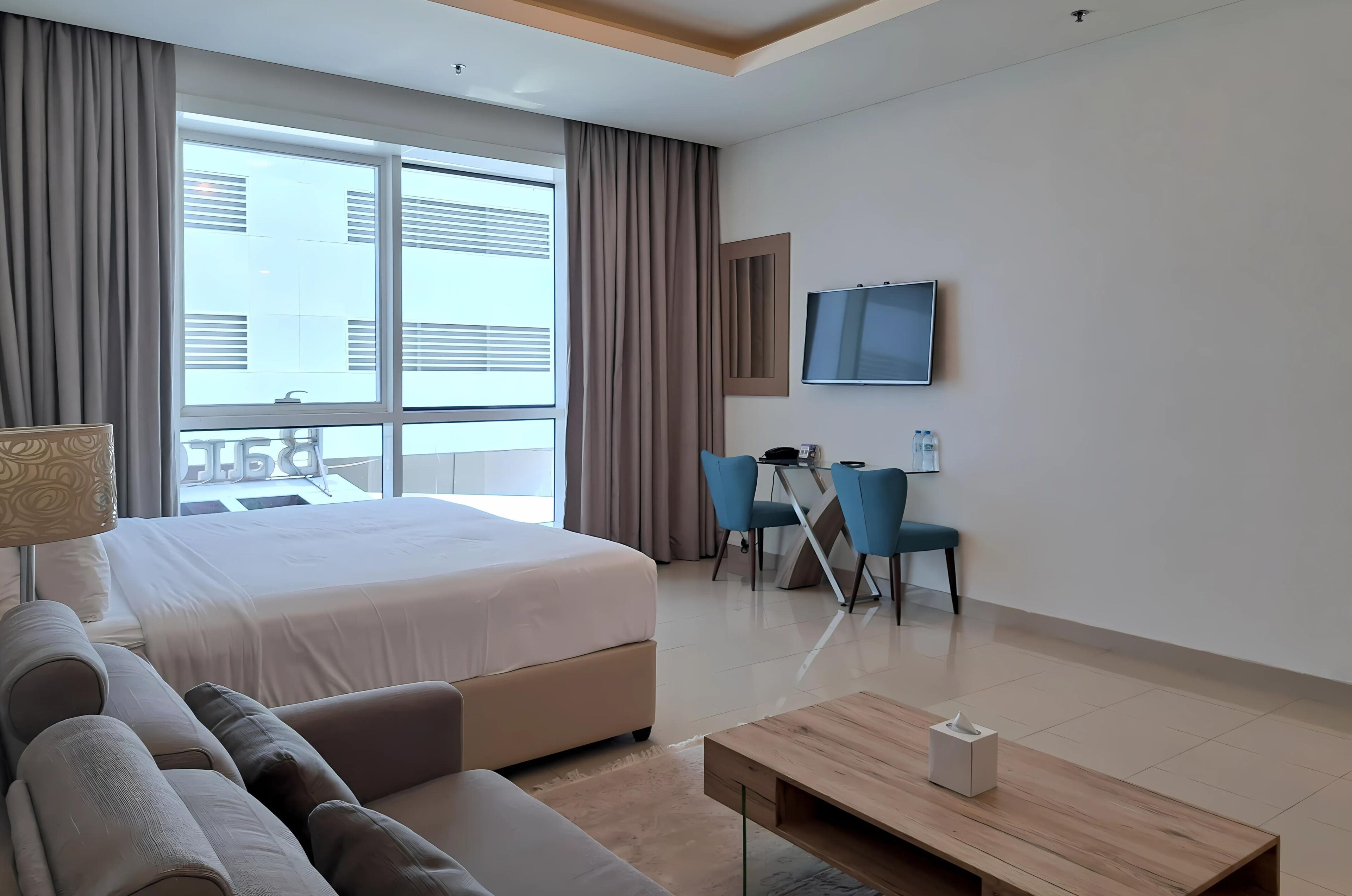 Une chambre d’hôtel comprenant un lit, un canapé, un bureau avec des chaises, une télévision et une fenêtre avec des rideaux.