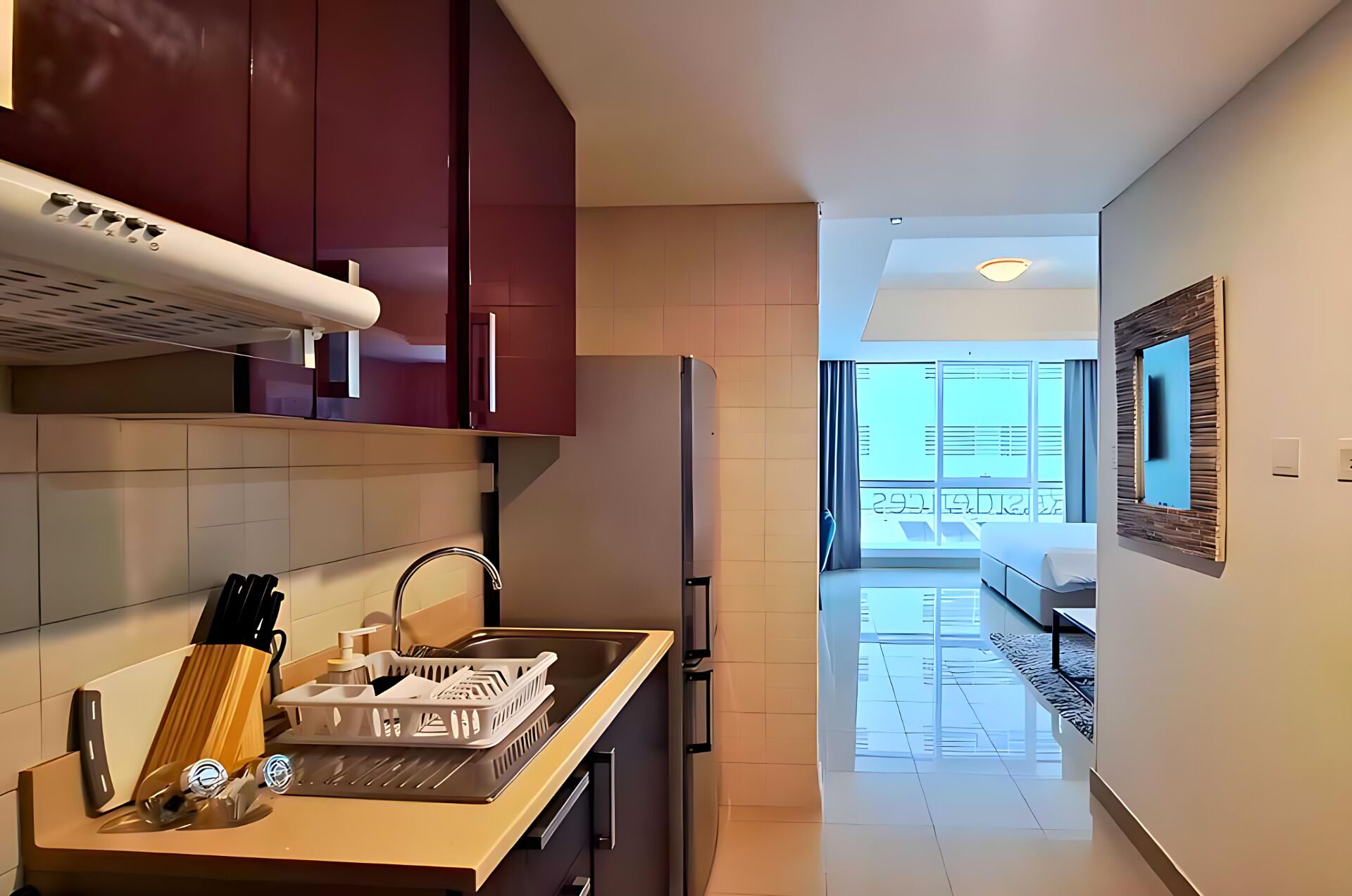 A modern kitchen with a built-in oven, a refrigerator, and a sink. There is a window with a view of the outside.