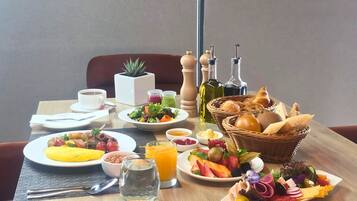 Uma mesa de café da manhã com pratos de comida, uma xícara de café, um copo de suco de laranja e uma cesta de pão.