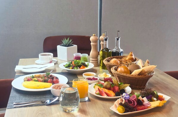 A breakfast table with plates of food, a cup of coffee, a glass of orange juice, and a basket of bread.