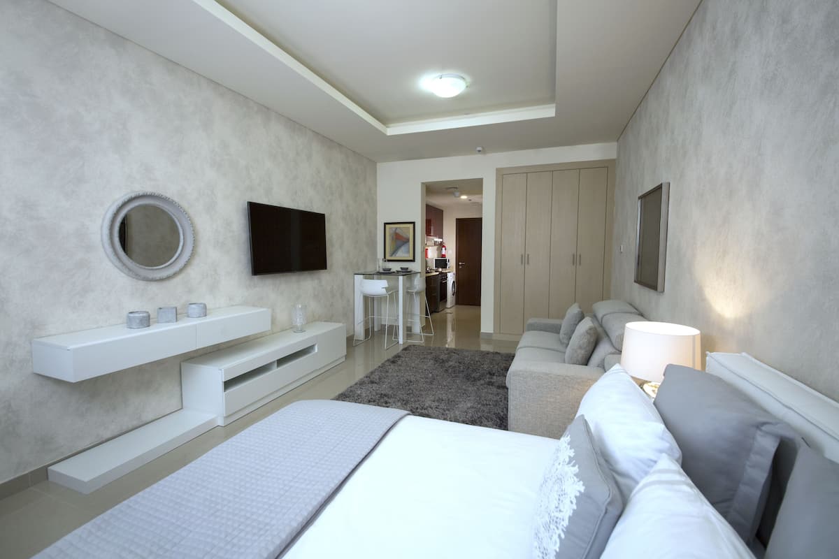 A modern bedroom with a large bed, a TV, a desk, and a wardrobe.