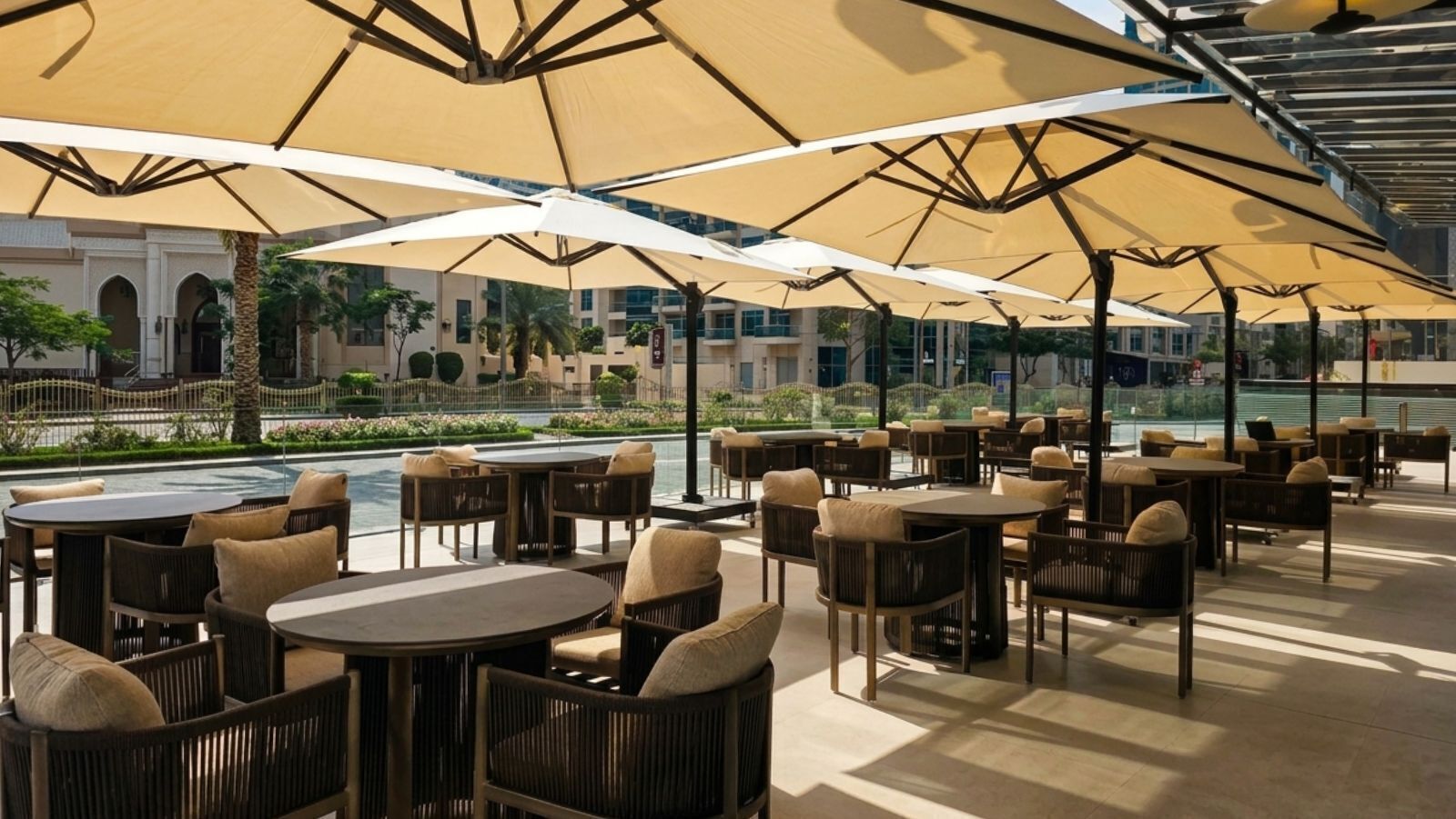 An outdoor seating area with tables and chairs, large umbrellas, and a pool in the background.
