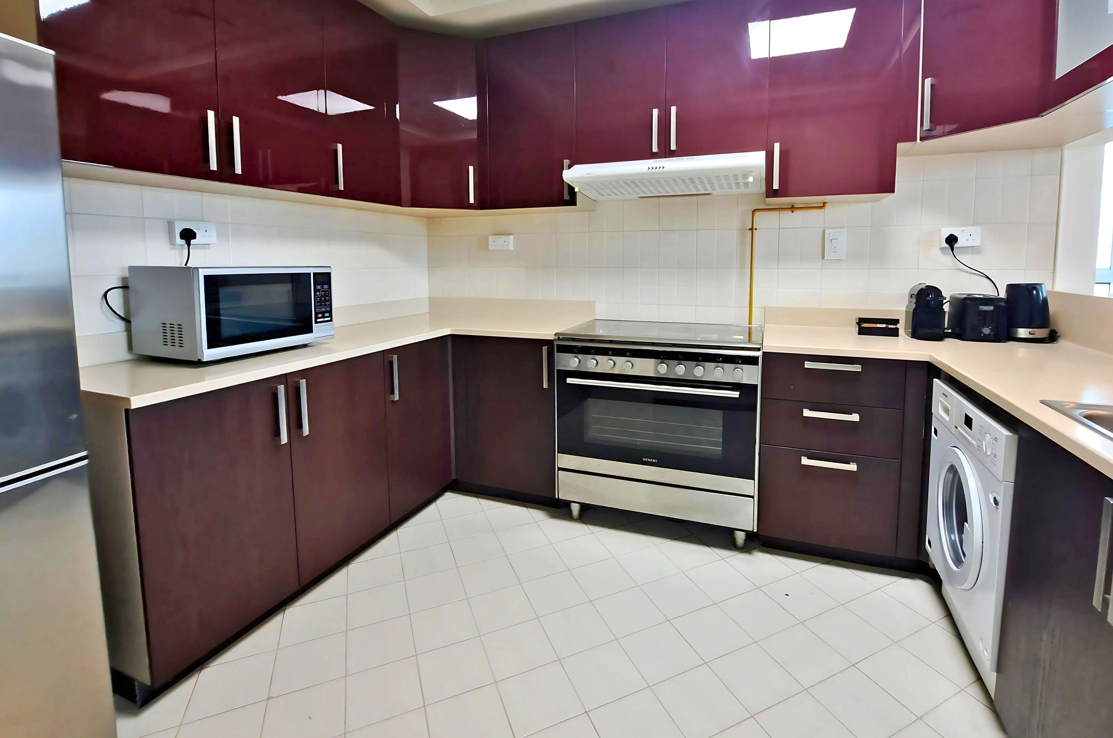 Een moderne keuken met donkerbruine kastjes, een magnetron, een oven, een wasmachine en een koffiezetapparaat.