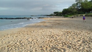 Una playa arenosa con huellas, una costa rocosa y una persona a lo lejos.