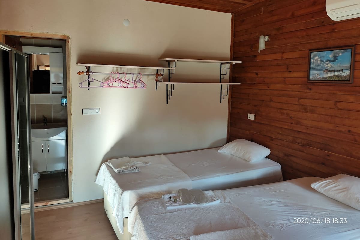 Quarto com duas camas, teto de madeira, banheiro com pia e um quadro na parede.