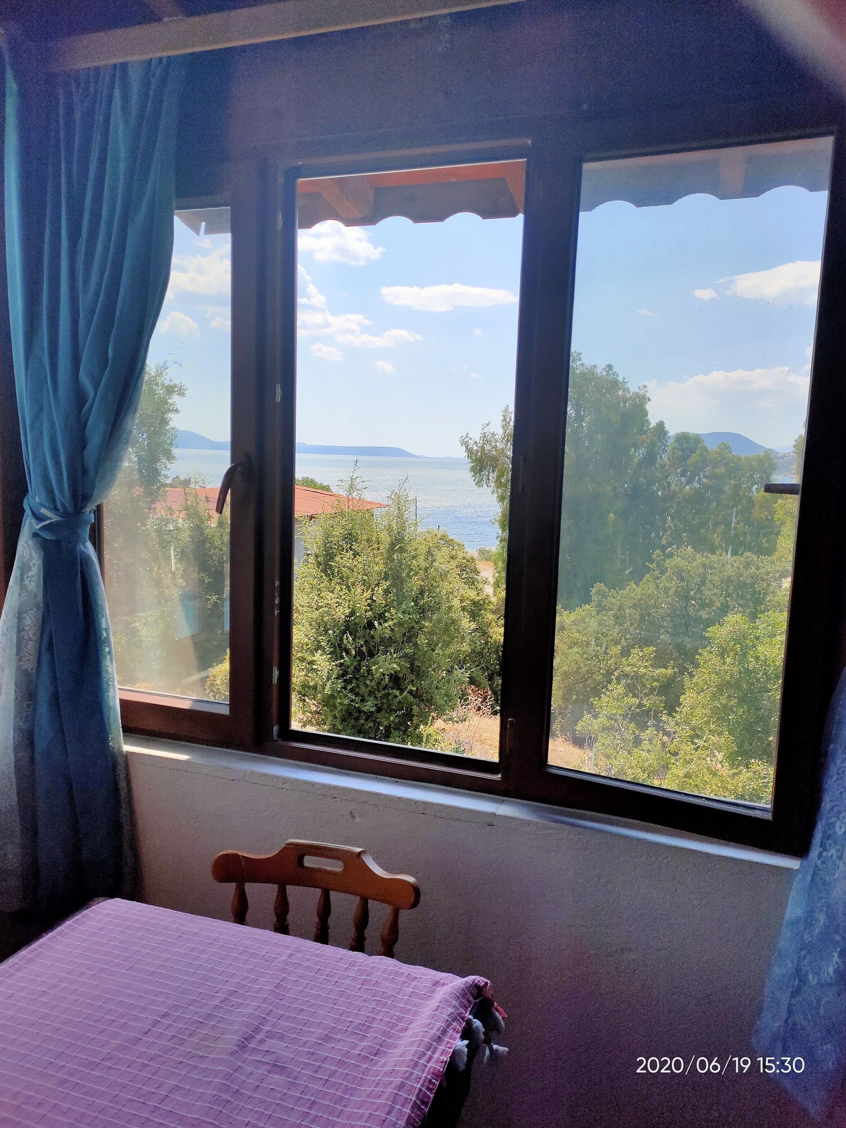 Una habitación con una cama, una silla de madera y un ventanal con vistas al agua y follaje.