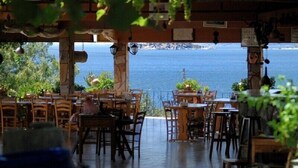 An outdoor restaurant with wooden tables and chairs, overlooking a body of water. - Selenes Pansiyon (Milas)