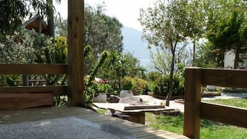 Eine Holzterrasse mit weißem Teppich, umgeben von Grünpflanzen und Blick auf ein Gewässer.