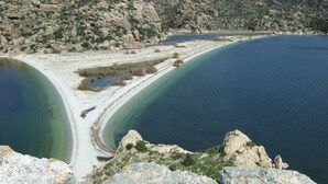 A coastal landscape with a sandy beach, clear blue waters, and rocky hills in the background. - Selenes Pansiyon (Milas)