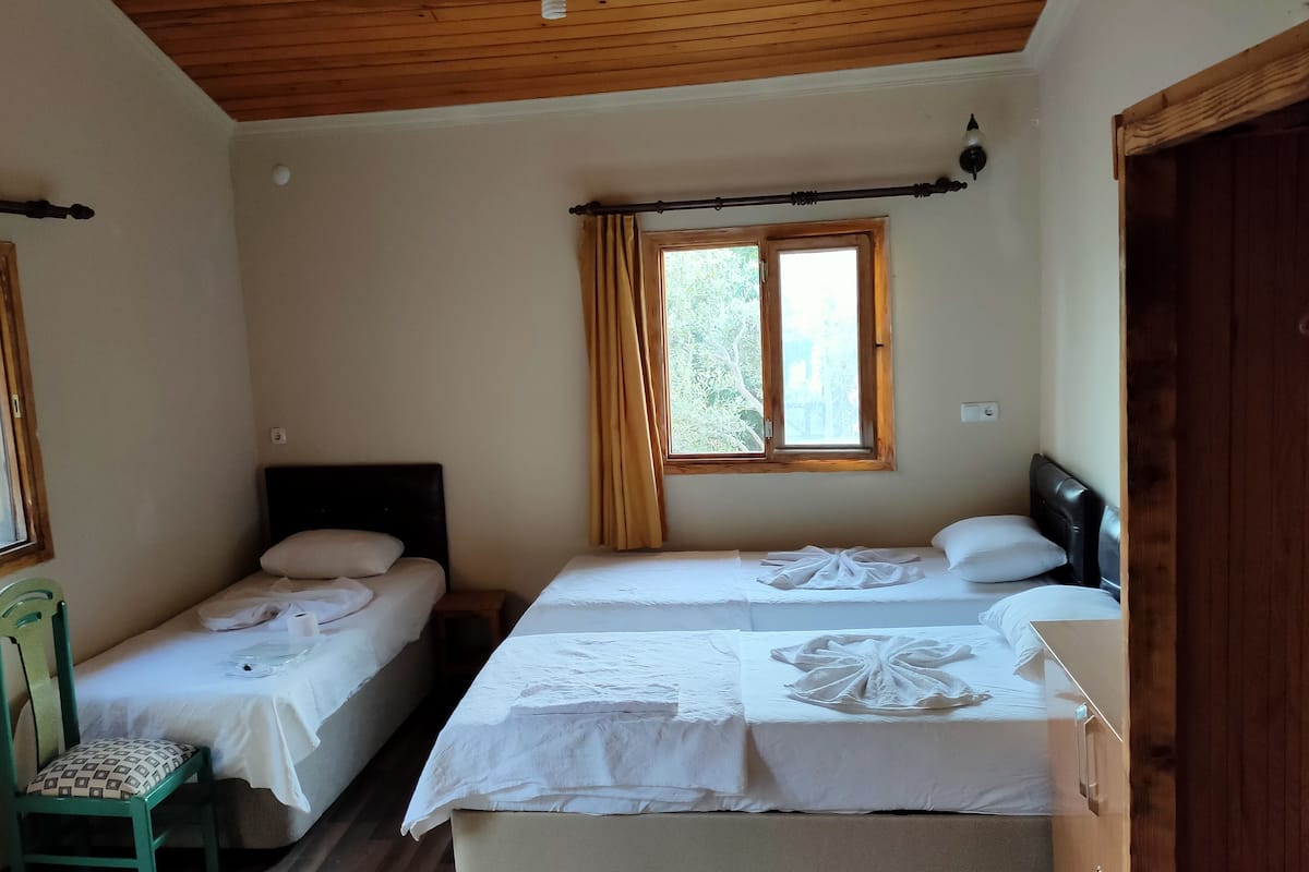 Quarto com duas camas de solteiro, teto de madeira, janela com cortinas e uma cadeira verde.