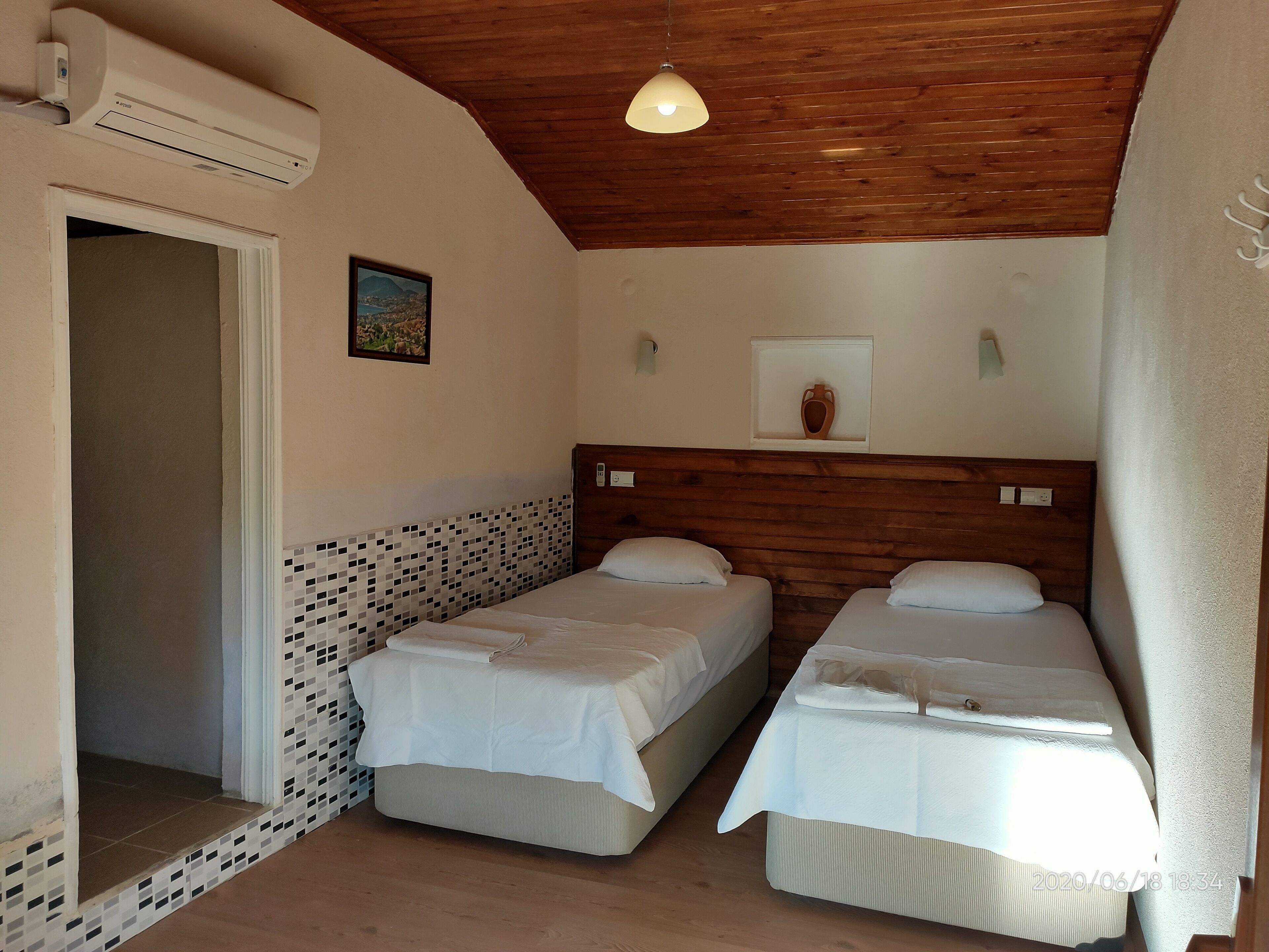 Una habitación con dos camas, techo de madera y un estante con un jarrón.