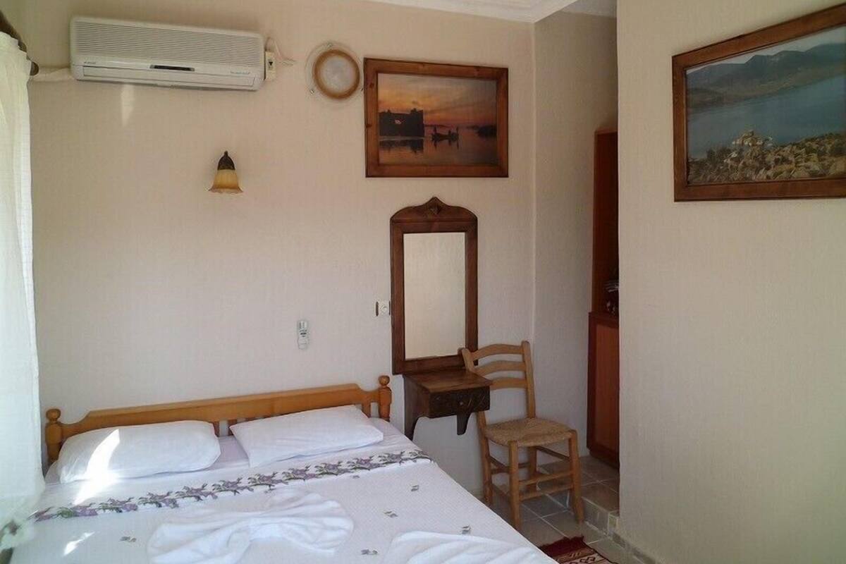 Quarto com cama, cadeira, escrivaninha, espelho, ar condicionado e um quadro na parede.