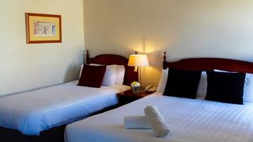 A hotel room with two single beds, a nightstand with a lamp, and a framed picture on the wall.