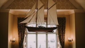 Un modelo de barco colgando del techo en una habitación con papel tapiz estampado y cortinas.