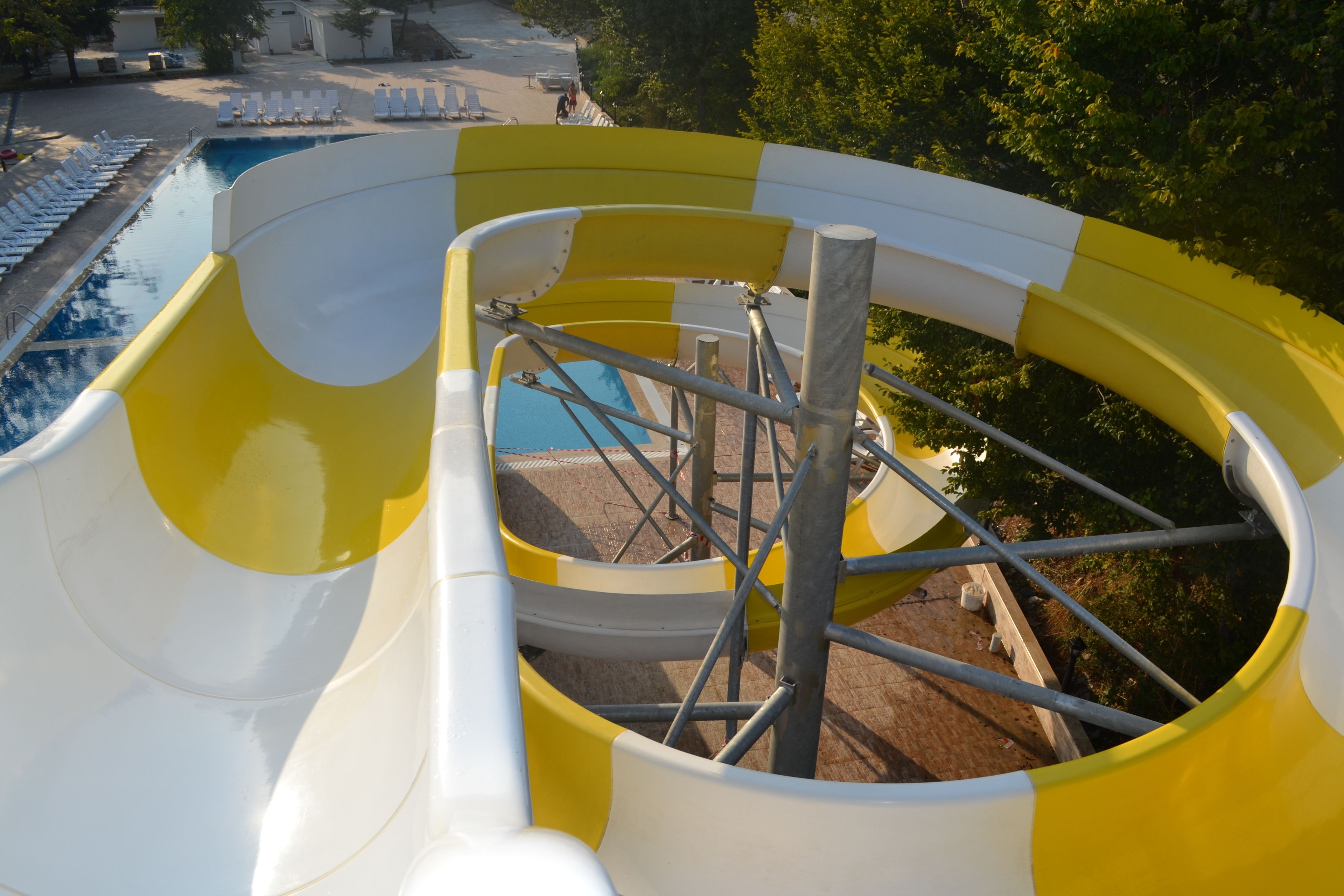 Un tobogán de colores amarillo y blanco, una piscina y sillas de descanso.