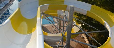 Un tobogán de colores amarillo y blanco, una piscina y sillas de descanso.