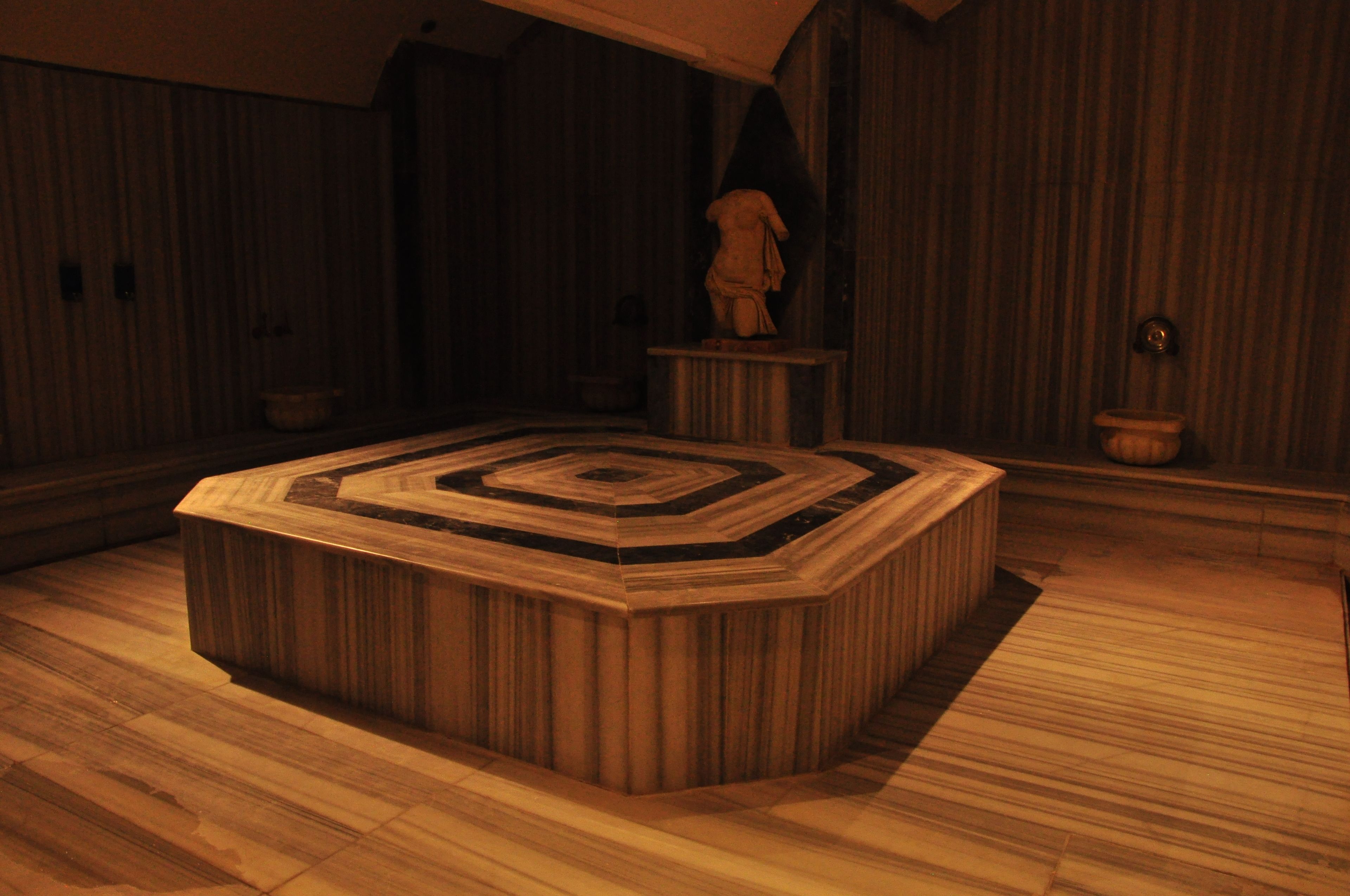 A room with a central octagonal wooden table, wooden walls, and a statue on a pedestal.
