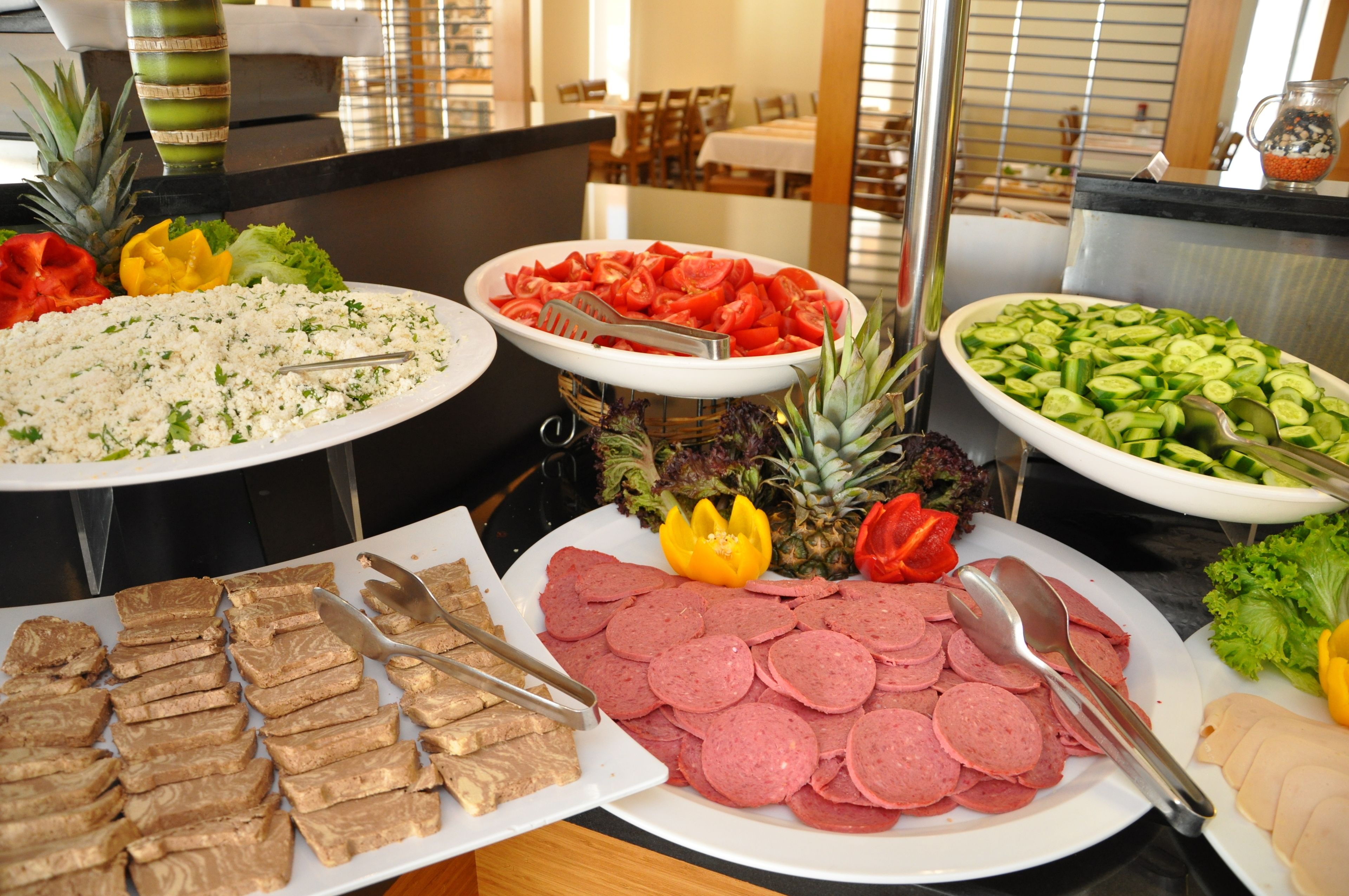 Ein Buffet mit verschiedenen Speisen, darunter Wurstwaren, Gemüse und Obst.