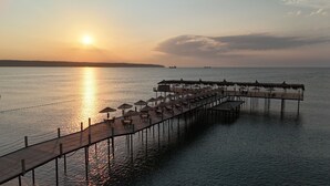 A pier with tables and umbrellas extending into calm water, a sunset in the background, and a distant shoreline. - Igneada Resort Hotel & Spa  (Demirköy)