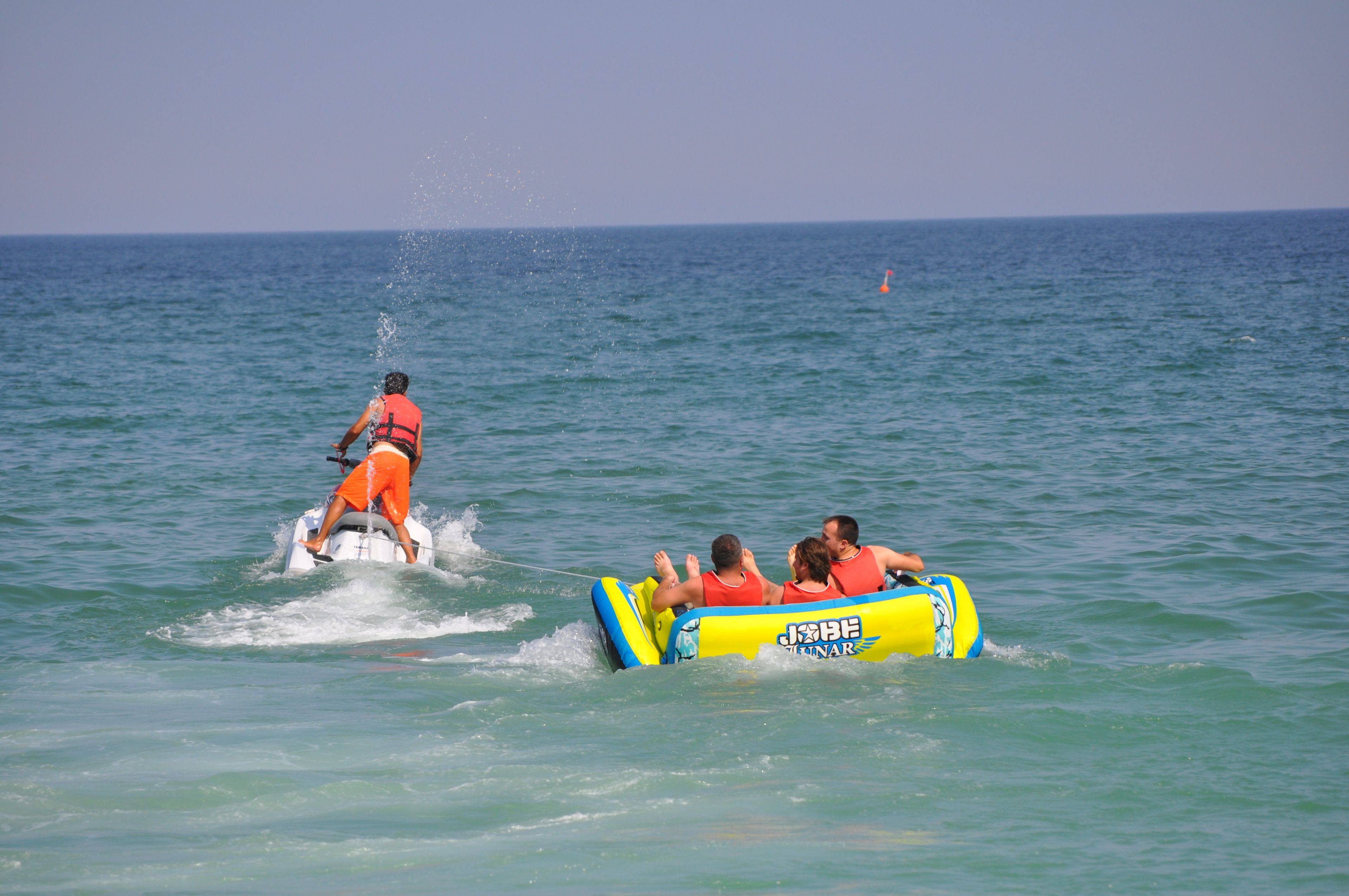 A water activity with a person on a jet ski and a group in a yellow inflatable raft.