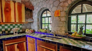 A kitchen with stone walls, wooden cabinets, and a checkered tile backsplash. - Villa Piton Caribbean Castle | Enhanced cleaning measures. CERTIFIED TO HOST!!! (Soufriere)