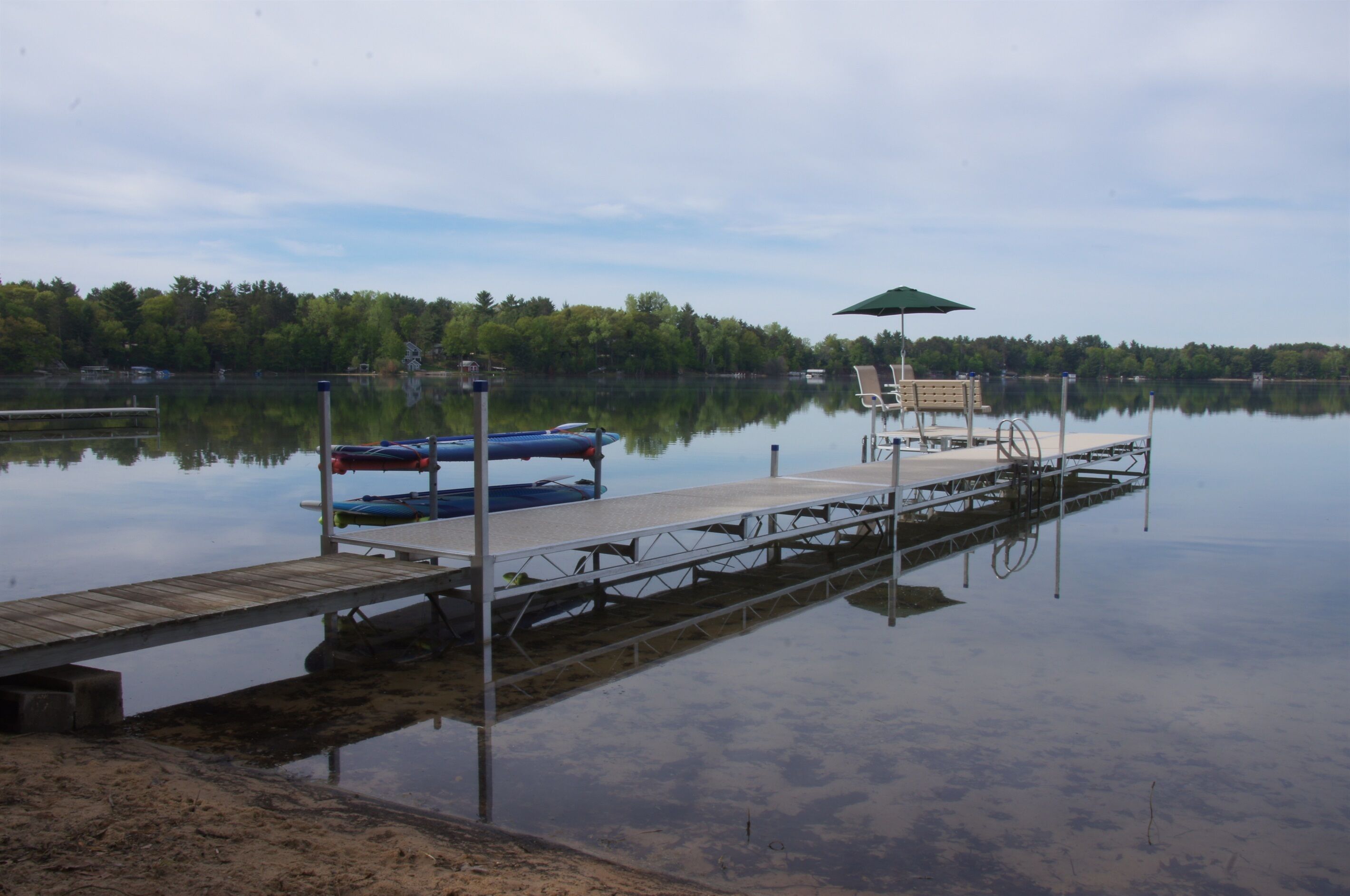 Un lac paisible avec un quai en bois, un bateau à rames et un banc équipé d’un parasol.