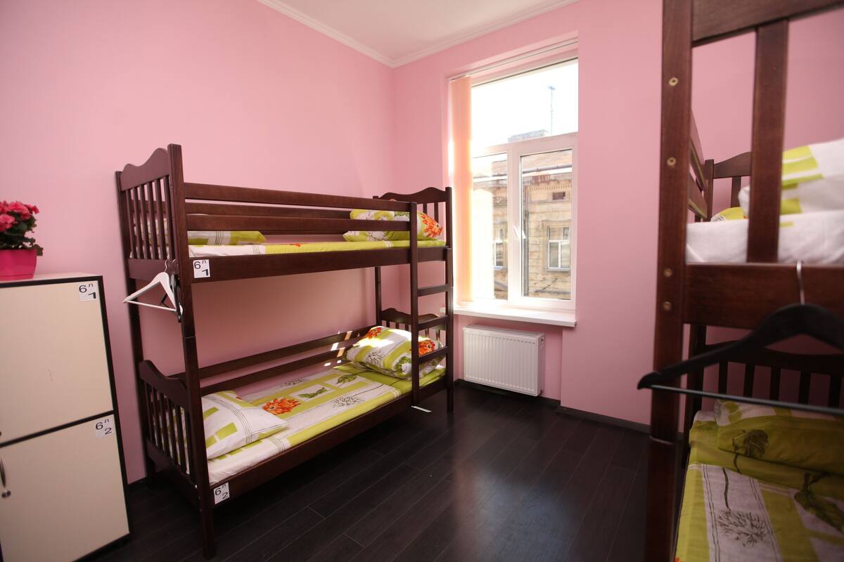 Habitación con literas, paredes rosas, una ventana y un radiador.