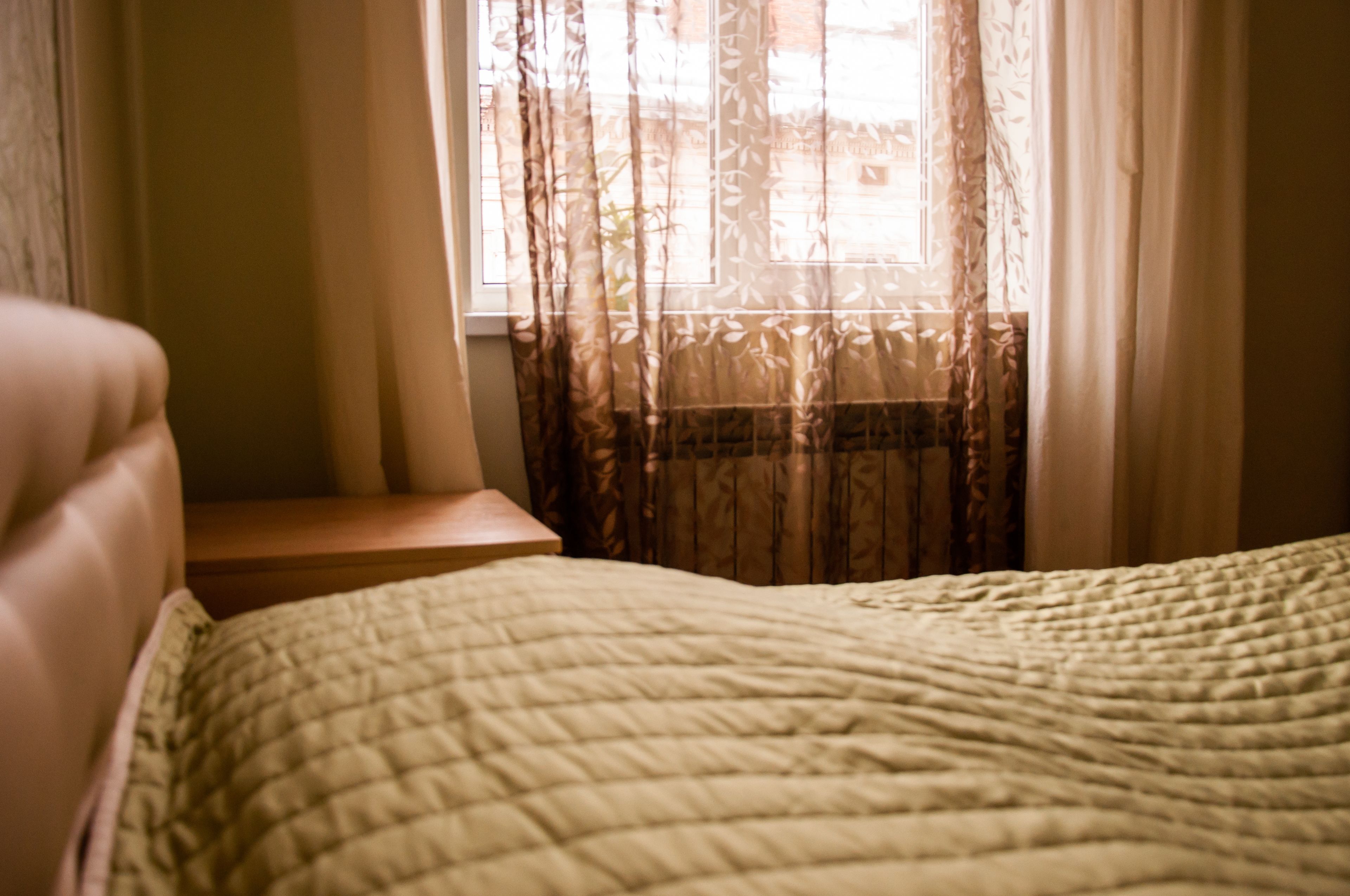 A bedroom with a bed, a nightstand, and a window with sheer curtains.