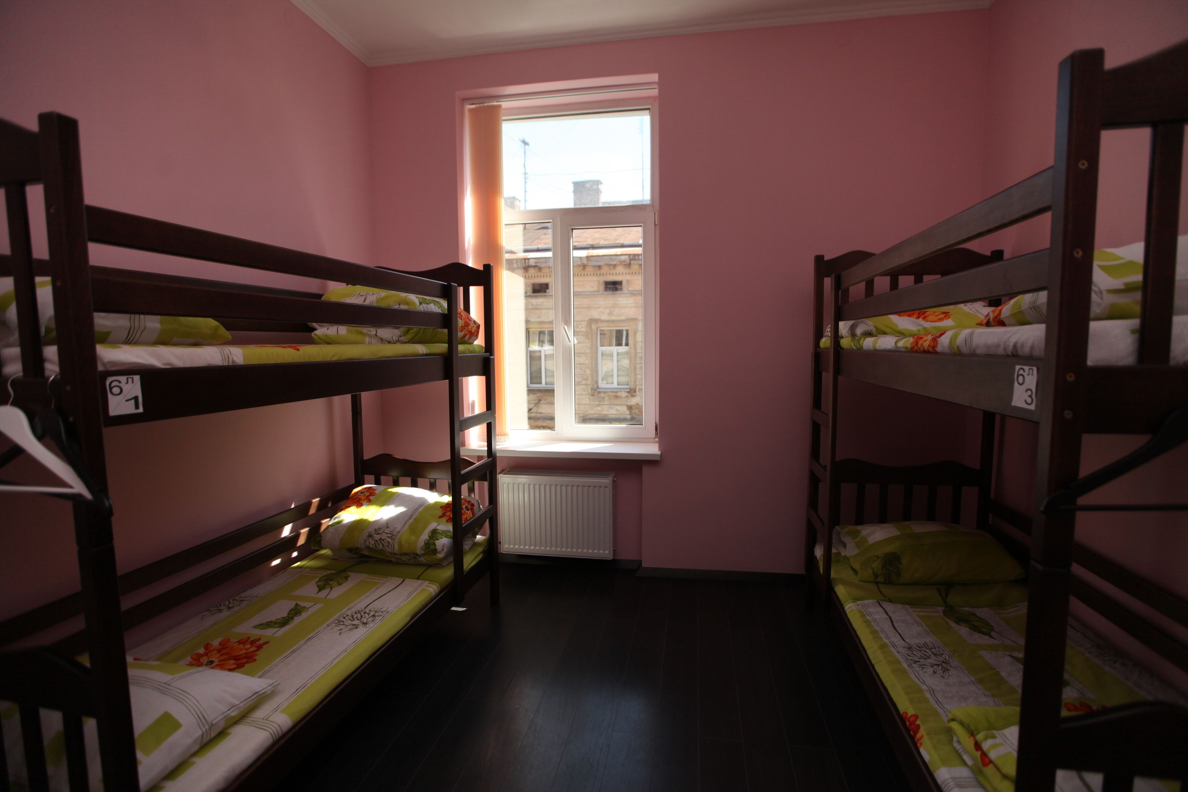 A dormitory room with bunk beds, a window with a view of buildings, and a radiator.