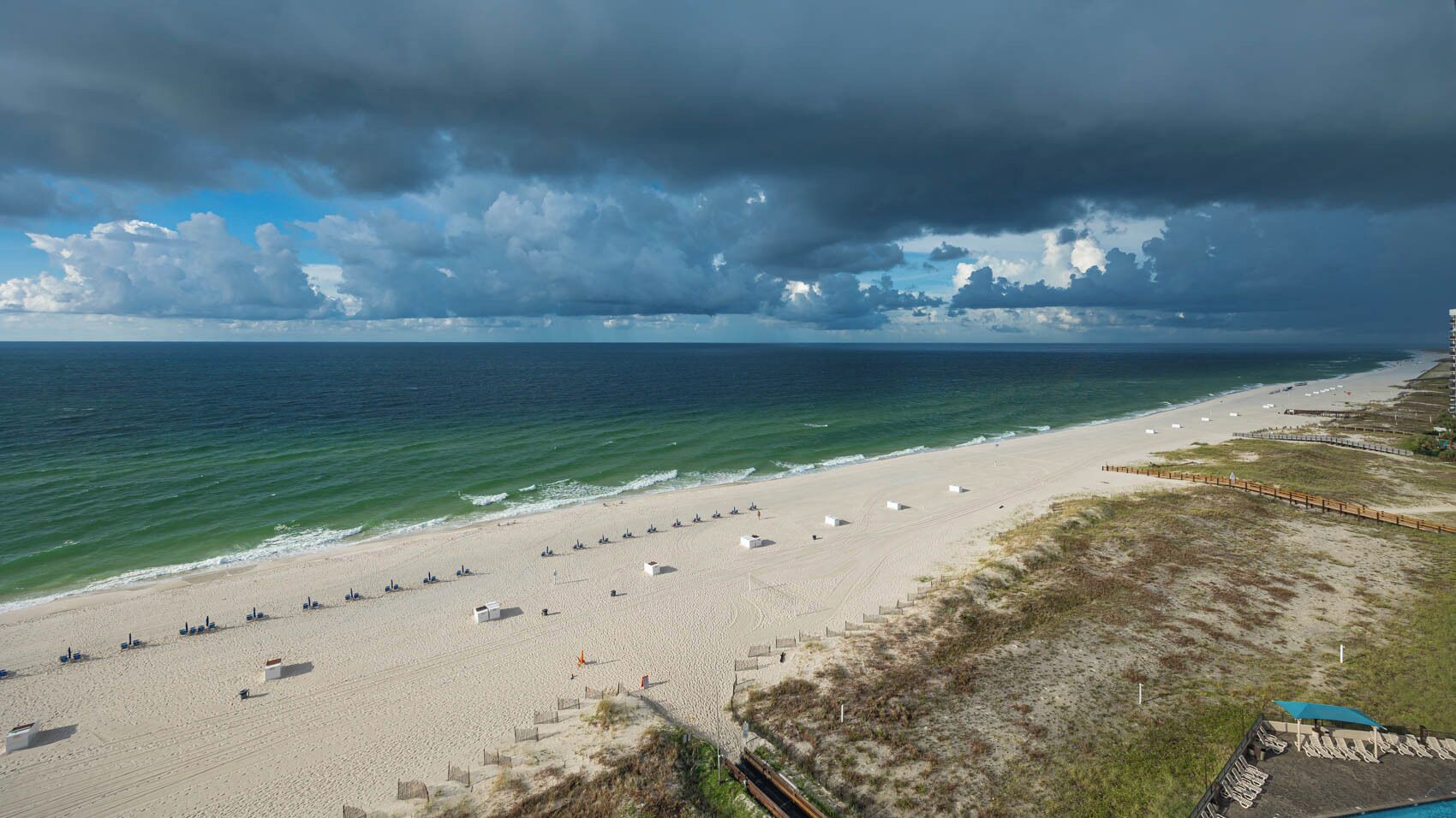 A beach with white tents and a wooden walkway along the shore.