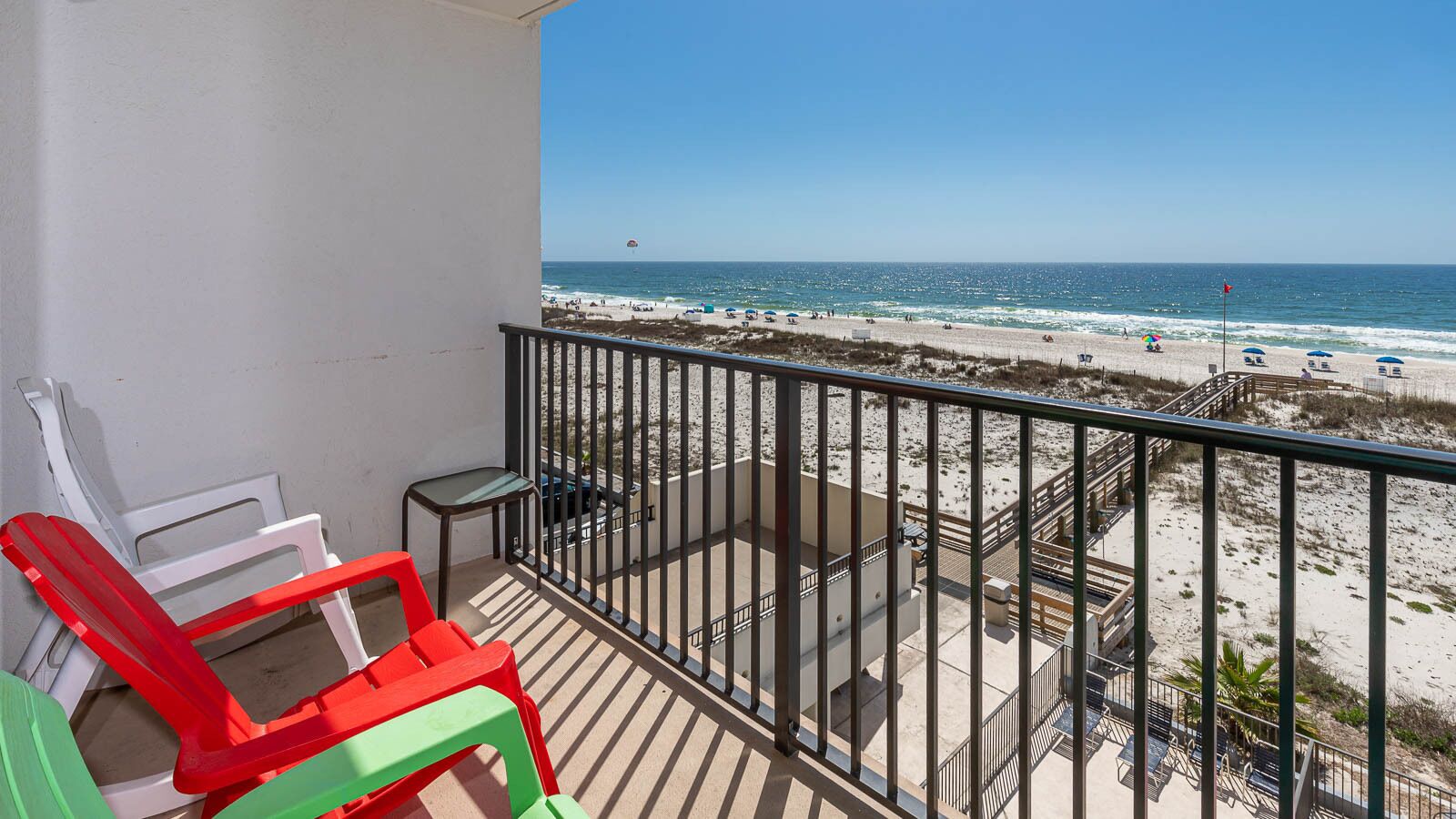 A balcony with a view of the beach, featuring a railing, a table, and two chairs.