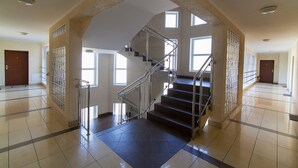 A spacious interior with a central staircase, large windows, and a tiled floor. - City Apartments - Apartamenty Młyńska 49 (Koszalin)