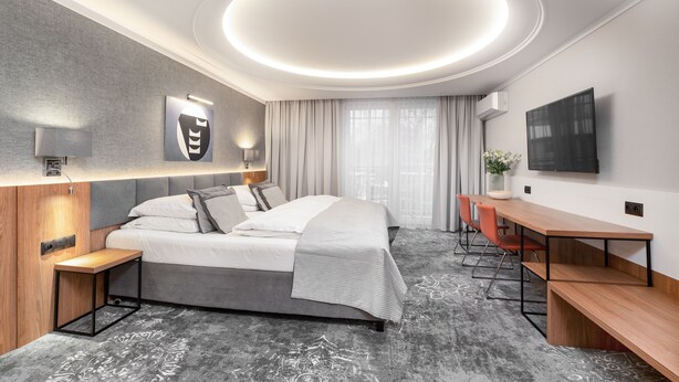 A modern hotel room with a large bed, a desk, and a TV. - City Apartments - Apartamenty Młyńska 49 (Koszalin)